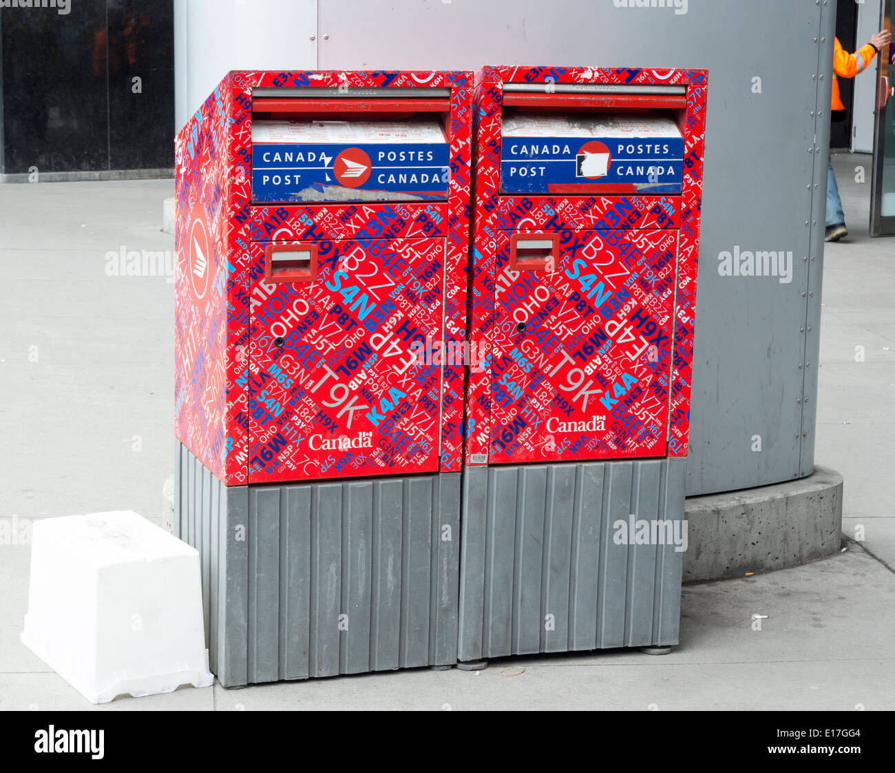 2 Canda Post Mailboxes covered in postal codes side by side in downtown Toronto with empty mail container next to them Stock Photo