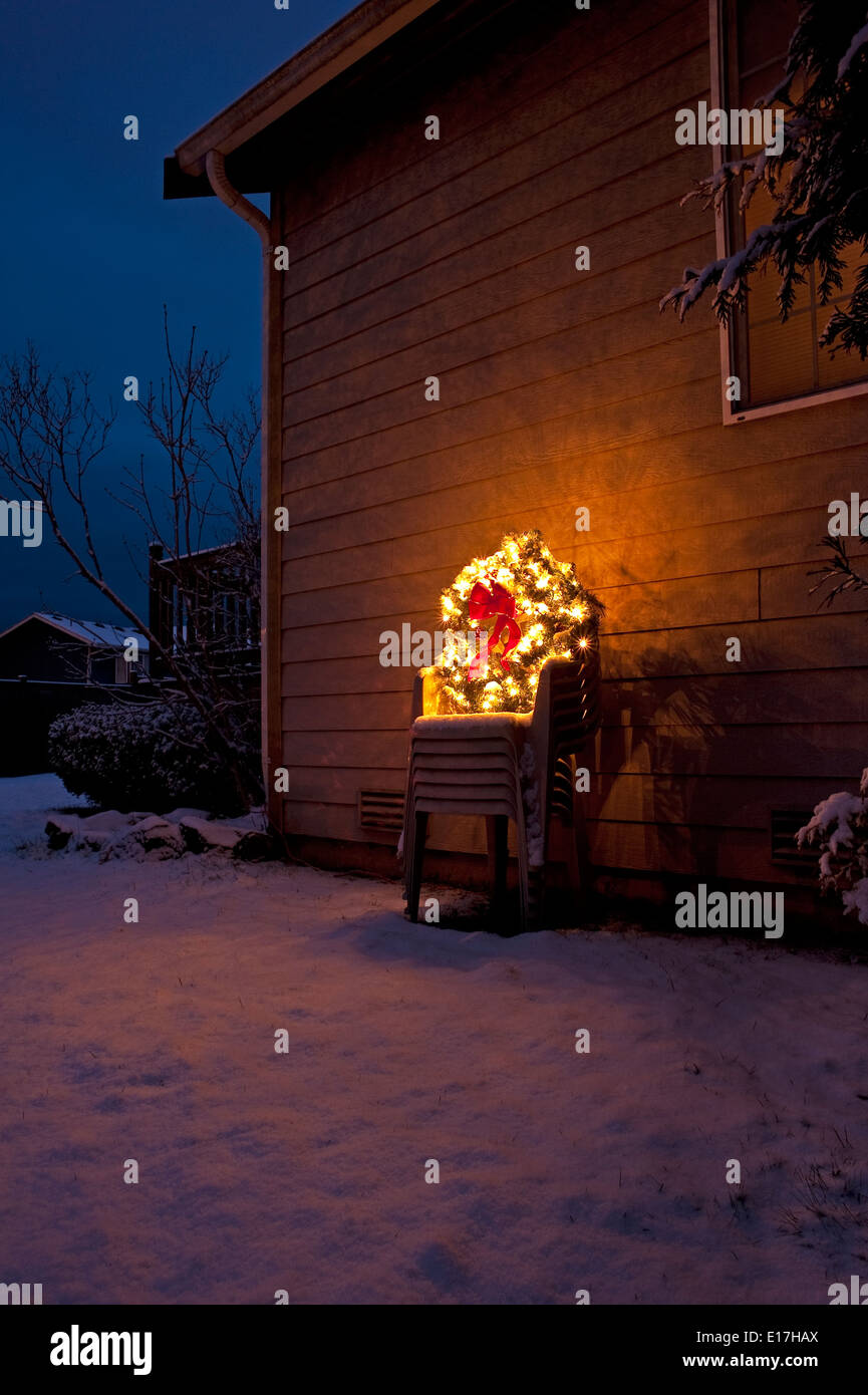 Christmas wreath in backyard on stacked lawn chairs with Christmas lights, red bow and snow Stock Photo