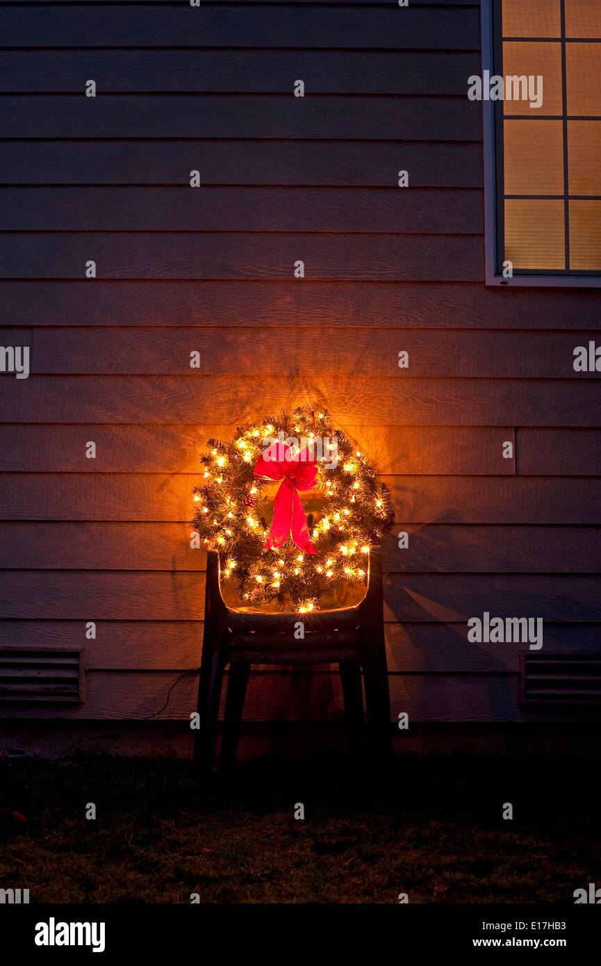Christmas wreath in backyard on stacked lawn chairs with Christmas lights and red bow Stock Photo