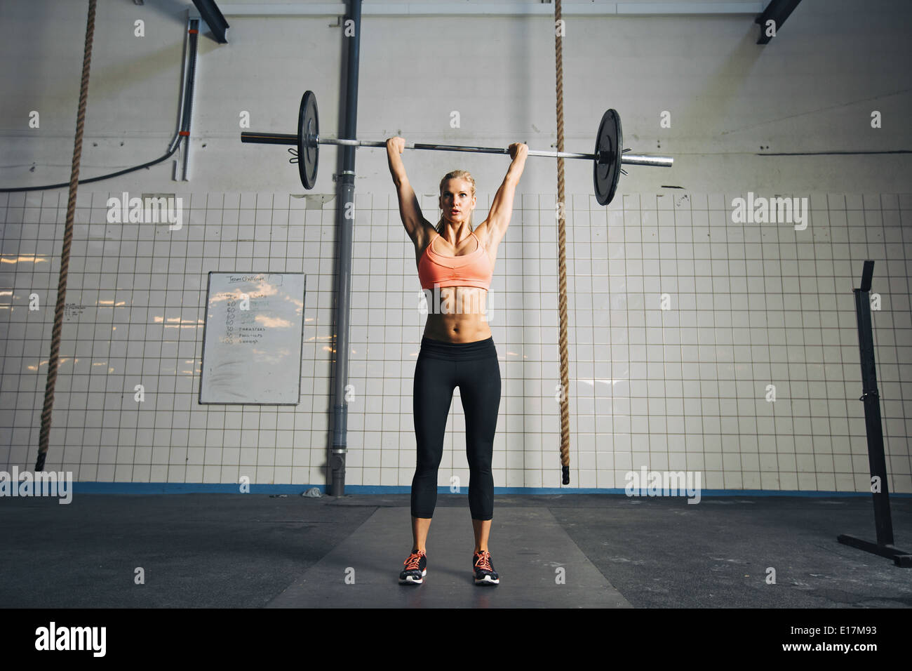 Full length image of strong young woman with barbell and weight plates overhead doing crossfit exercise. Fit female athlete. Stock Photo