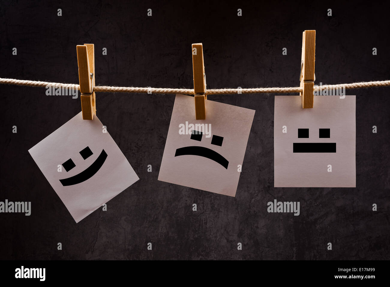 Emoticons printed on note paper attched to rope with clothes pins - happy, sad and neutral. Stock Photo