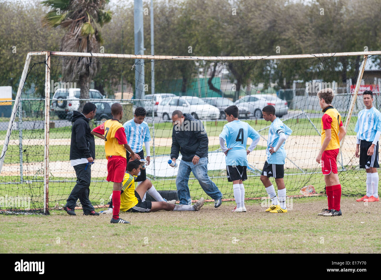 Injured junior football goalkeeper receiving treatment, players watching, Cape Town, South Africa Stock Photo