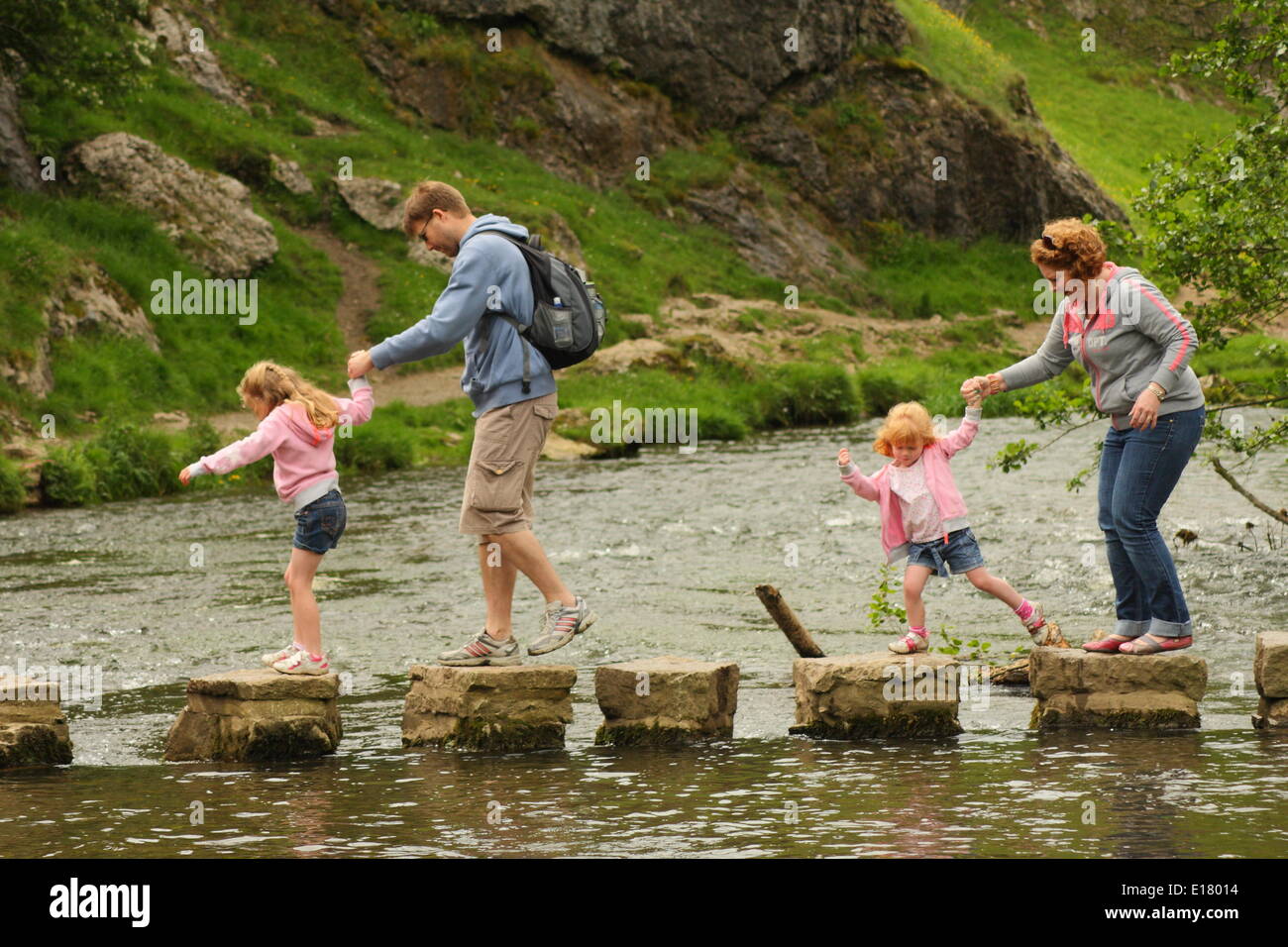 A family crosses the stepping stones of the River Dove at Dovedale in the Manifold Valley,Peak District, Derbyshire, England, UK Stock Photo