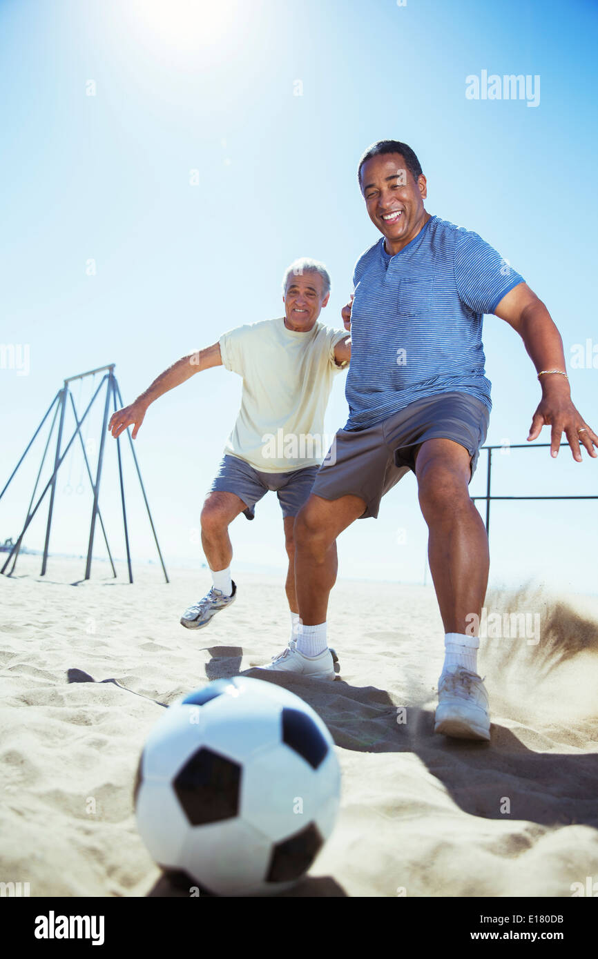 Senior men playing soccer on beach Stock Photo