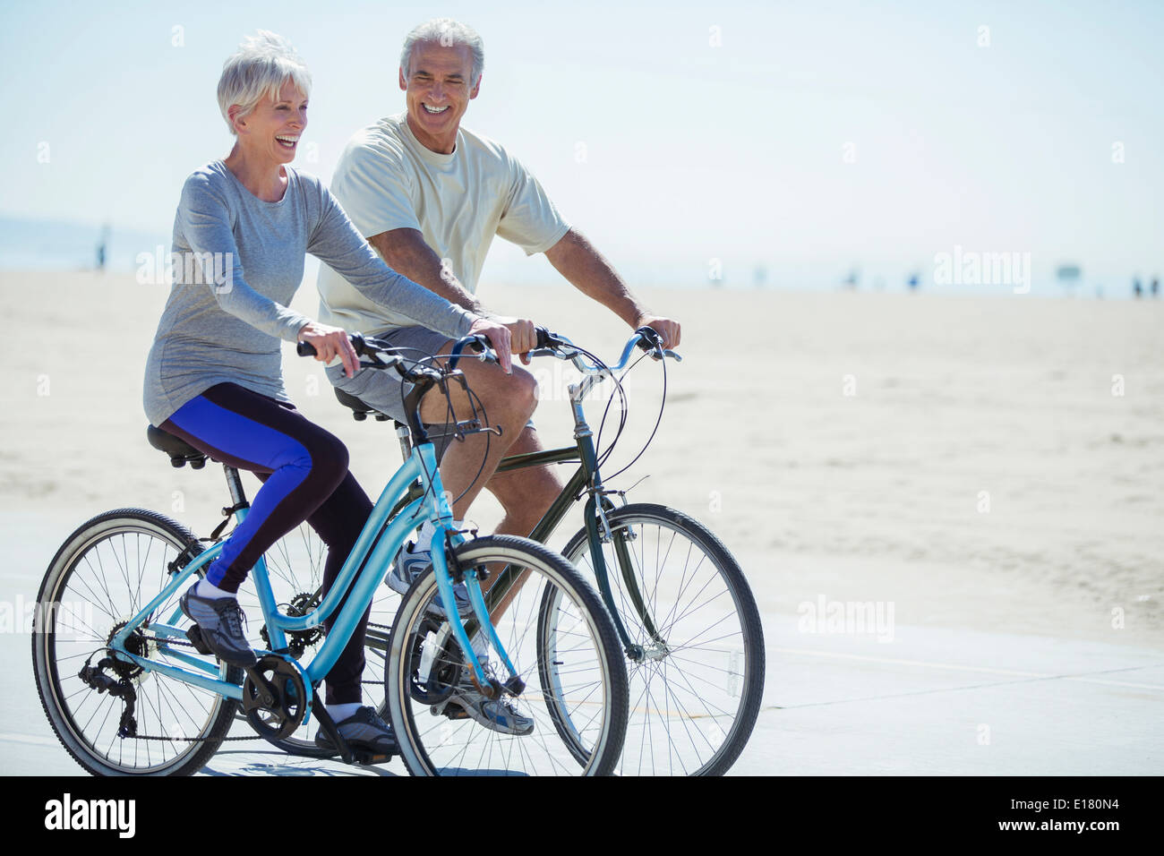 Senior couple riding bicycles on beach boardwalk Stock Photo