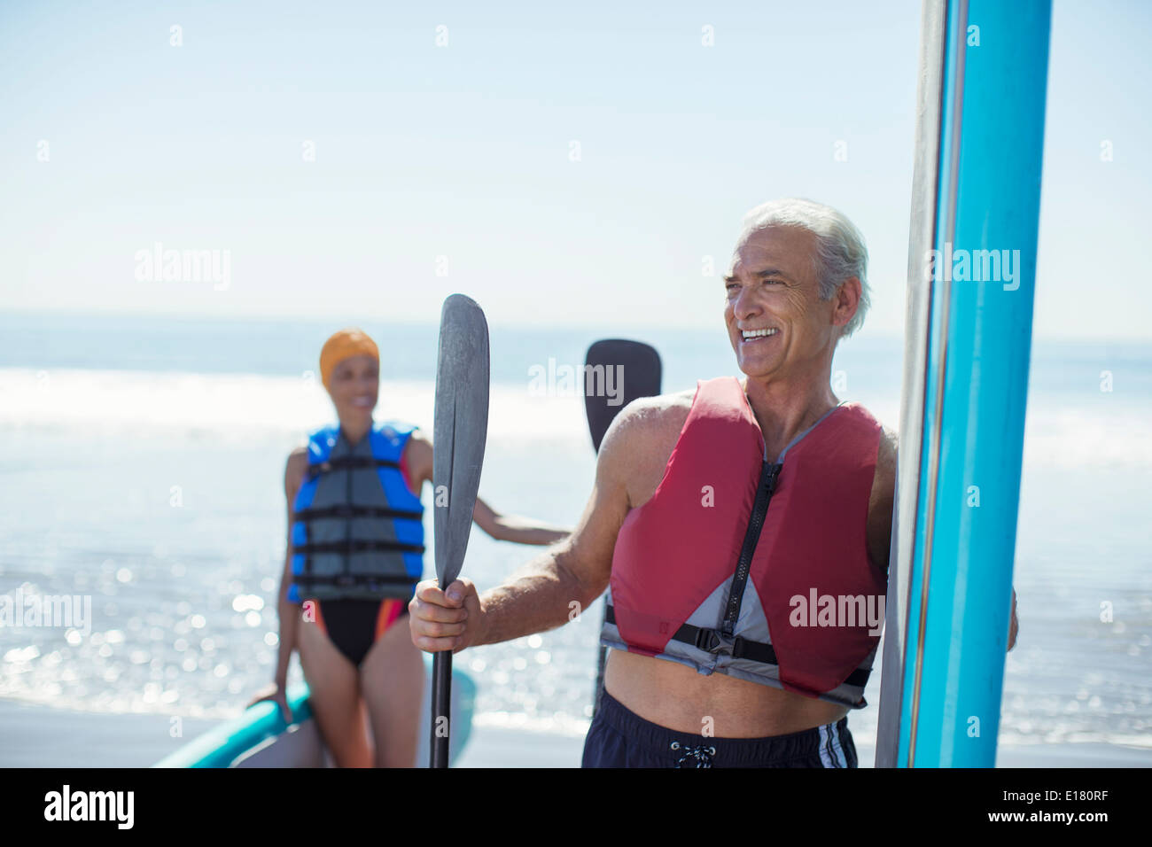 Senior couple with paddleboards on beach Stock Photo