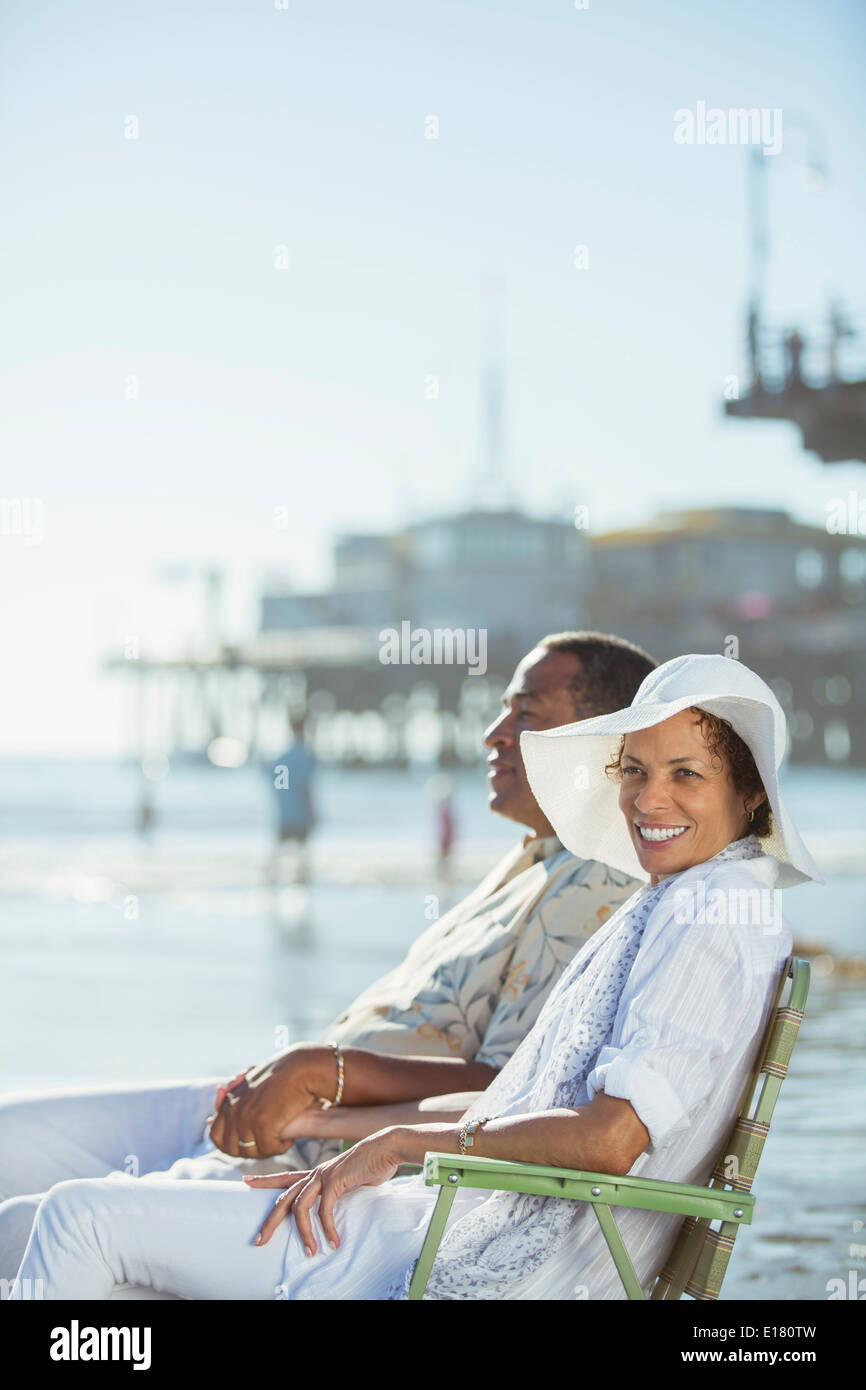 Portrait of couple relaxing in lawn chairs on sunny beach Stock Photo