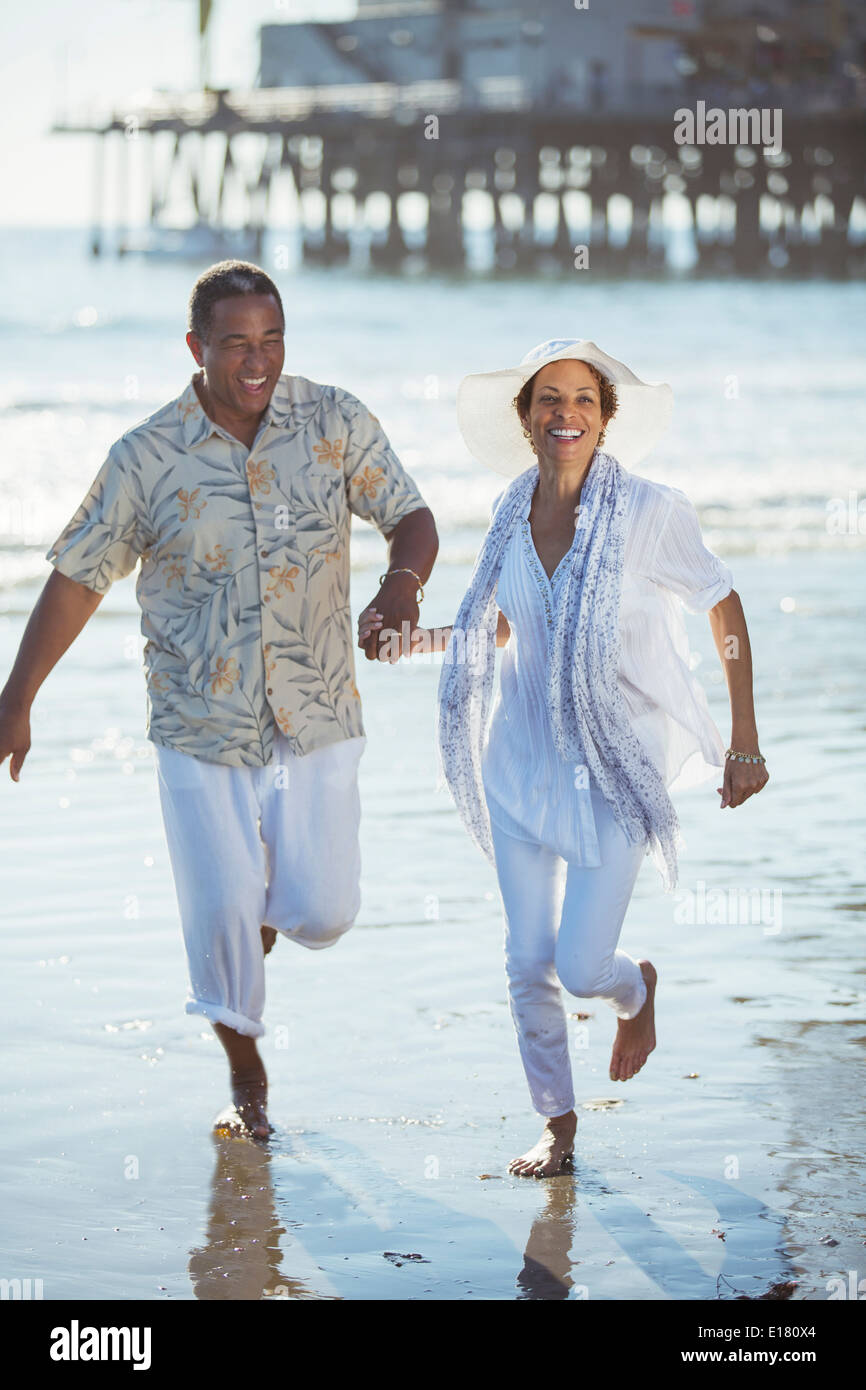 Smiling senior couple running on sunny beach Stock Photo