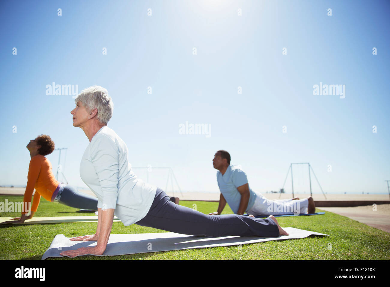 Seniors practicing yoga in sunny beach park Stock Photo