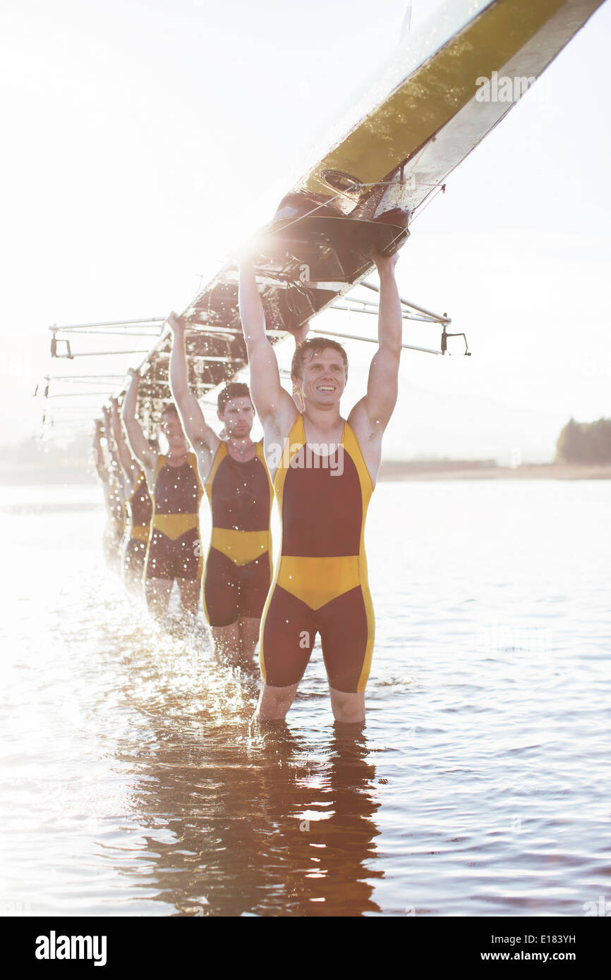 Rowing team carrying scull overhead in lake Stock Photo