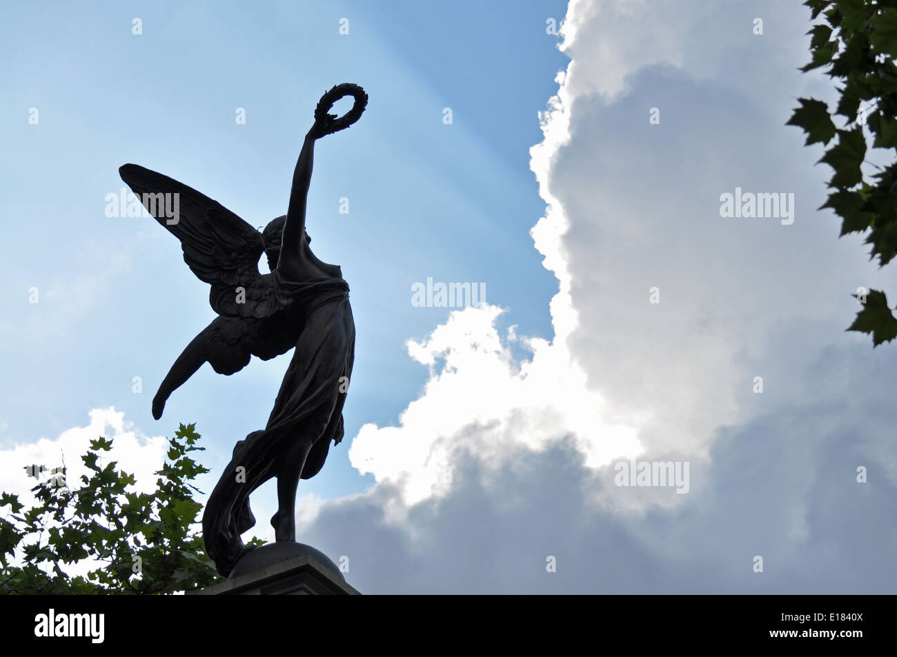 Shafts of light from the sun break through the clouds behind a statue of Victory on a war memorial near sunset Stock Photo