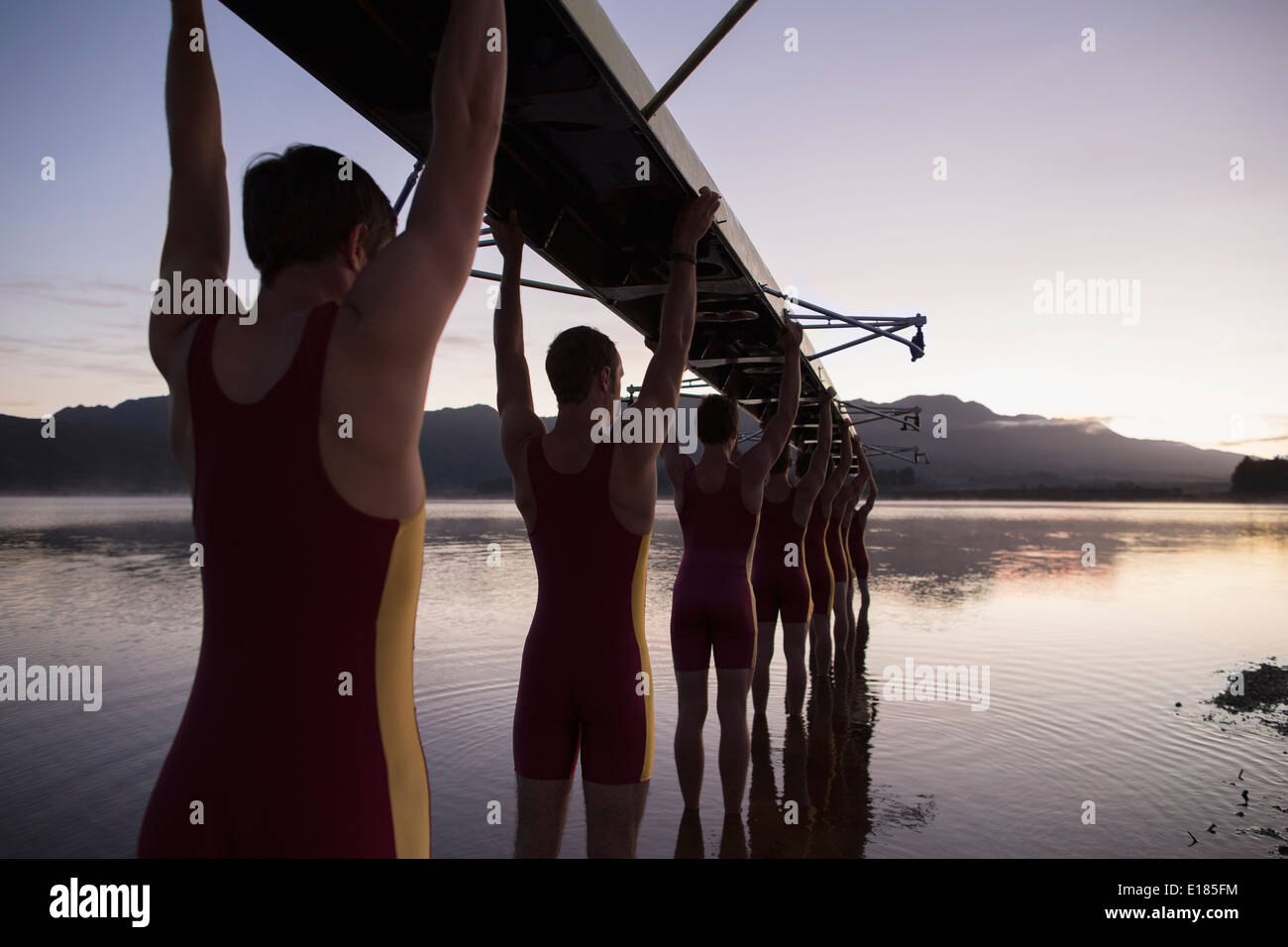 Rowing team carrying boat overhead into lake Stock Photo