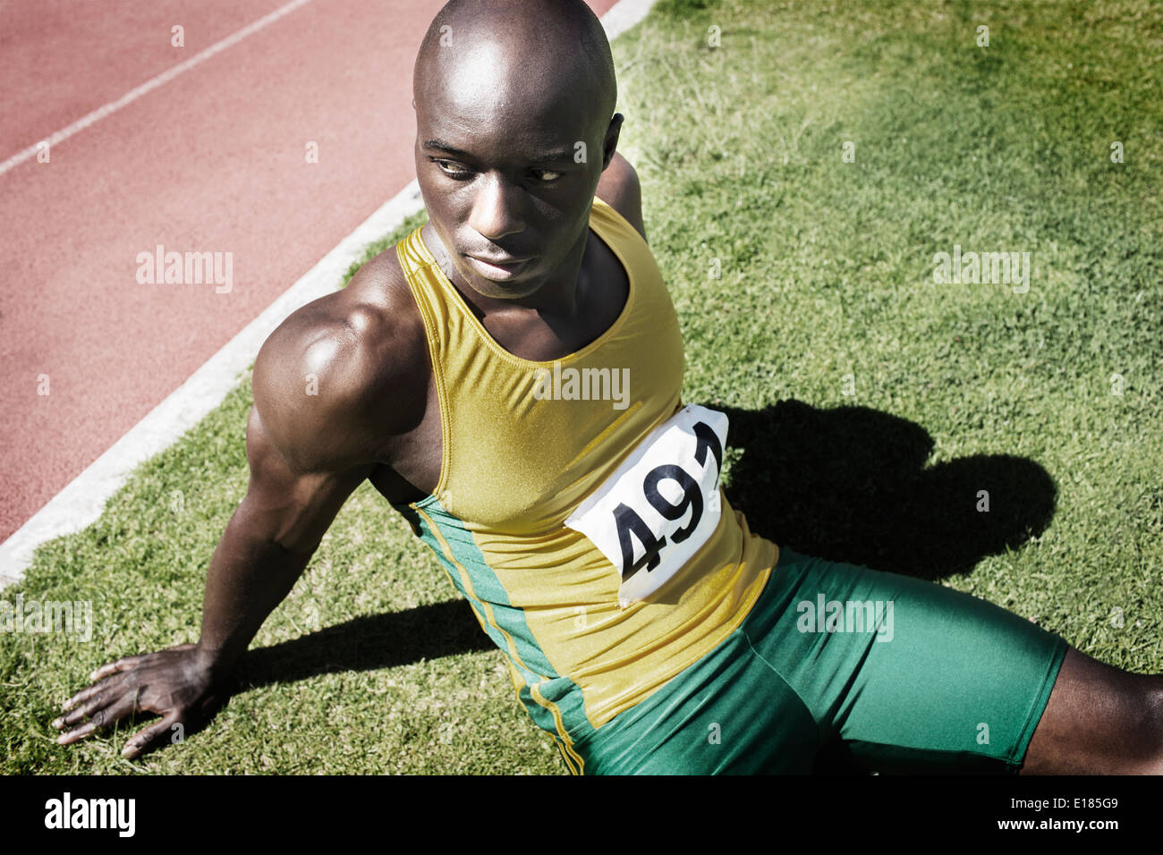 Athlete resting in grass next to running track Stock Photo