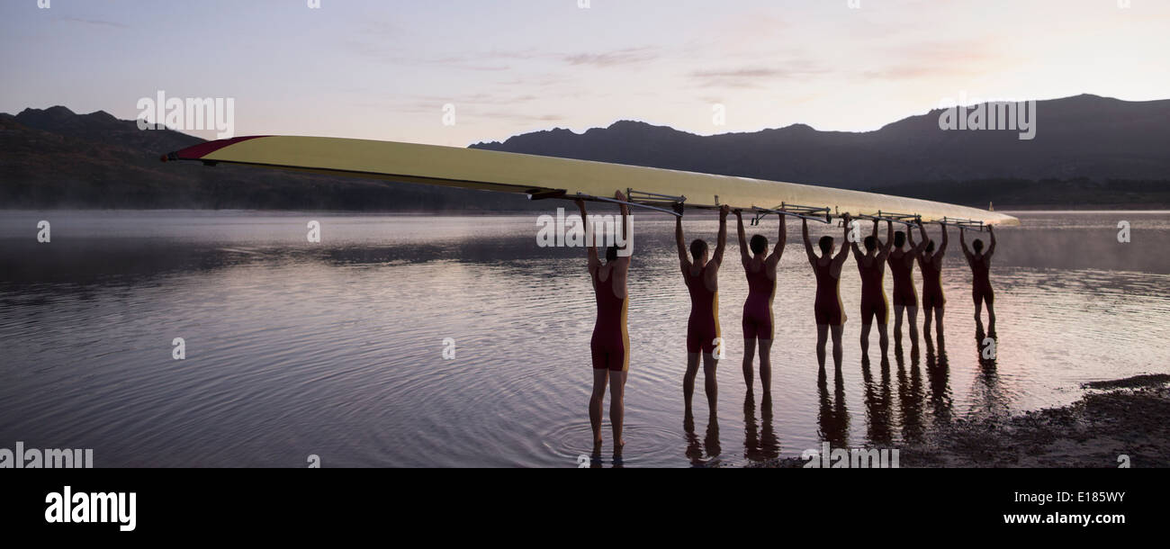Rowing crew holding scull overhead in lake Stock Photo