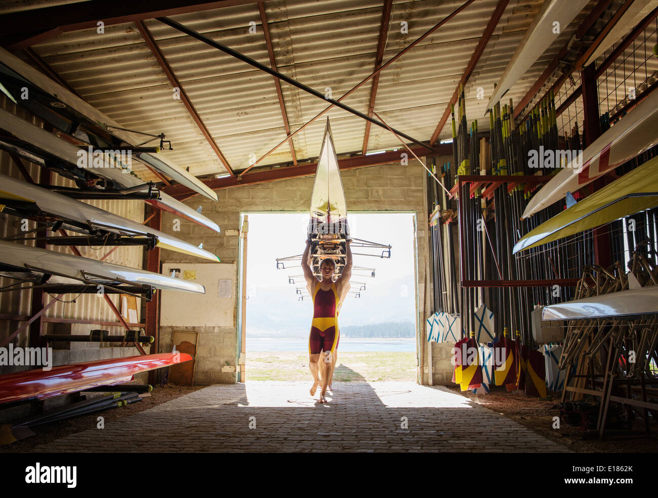 Rowing team carrying scull into shed Stock Photo