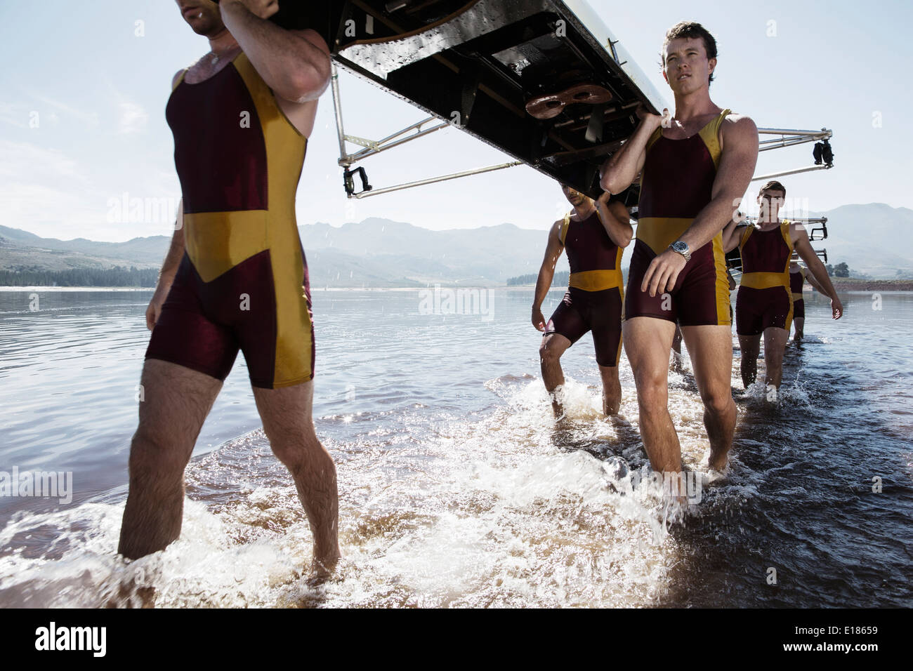 Rowing team carrying scull out of lake Stock Photo