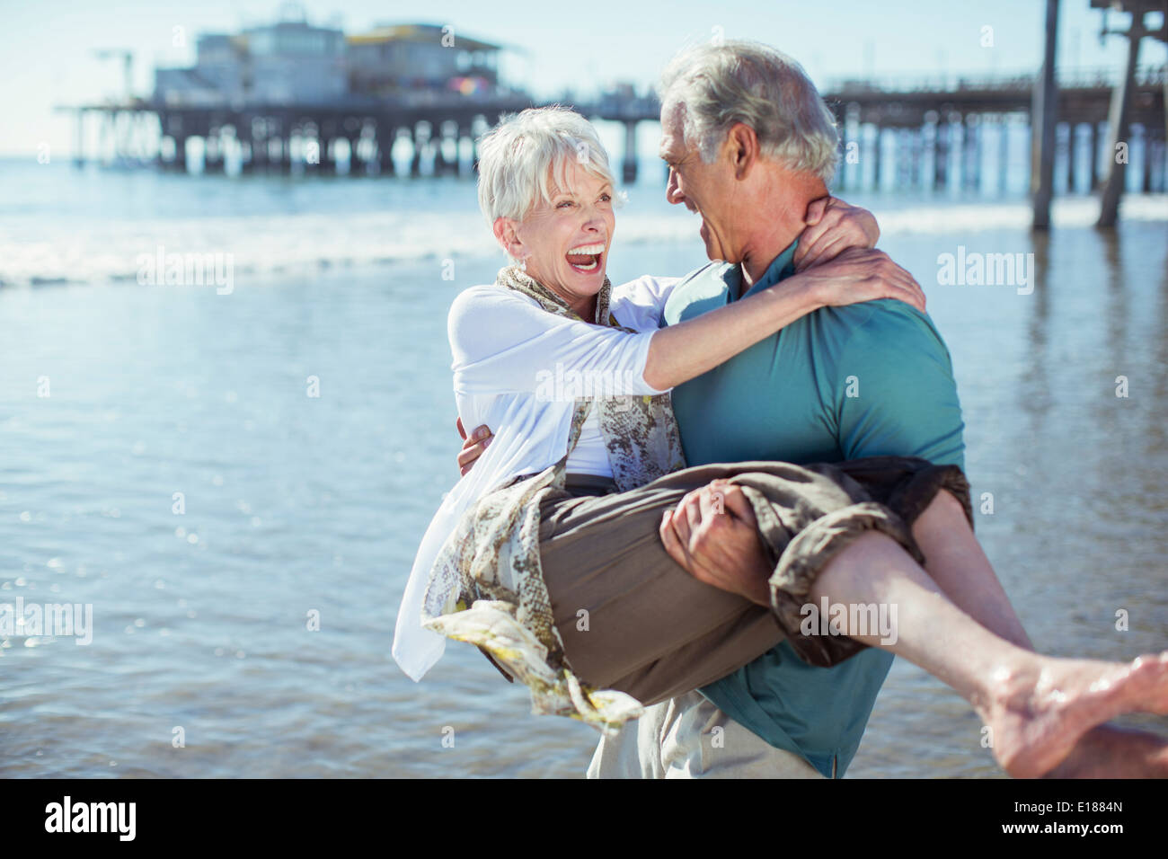 Senior man carrying wife on sunny beach Stock Photo