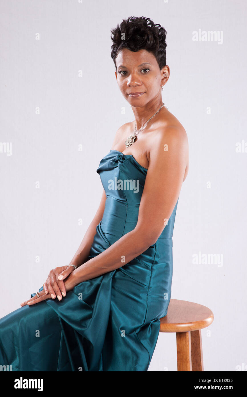 Pretty black woman in  dress without shoulders, sitting and smiling at the camera with a friendly, pleased, expression Stock Photo