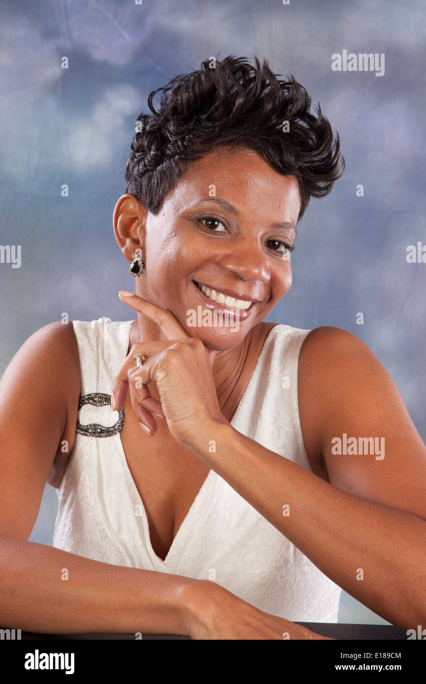 Pretty black woman in white dress, with her hand on her chin, smiling at the camera with pleasure and joy Stock Photo