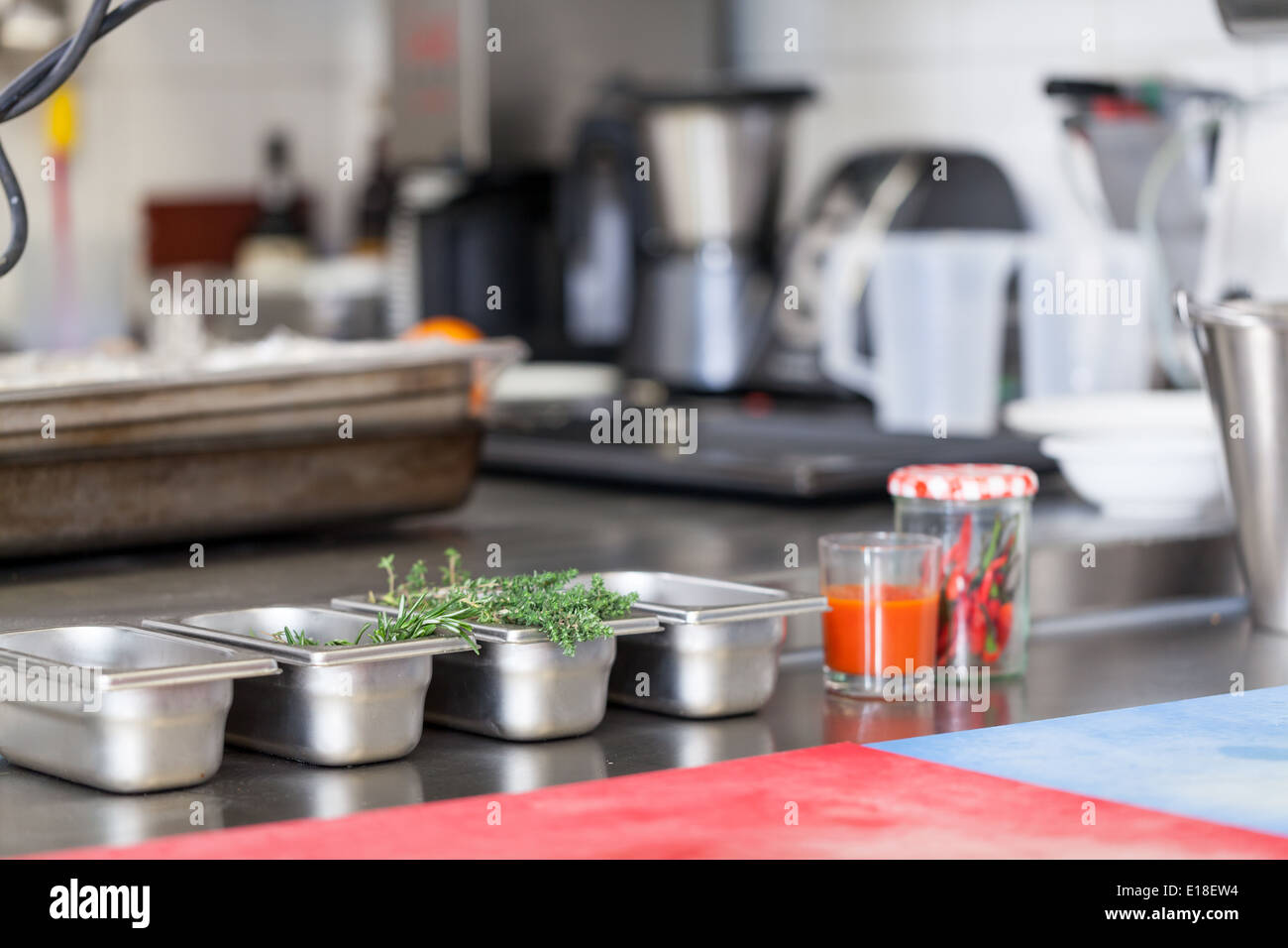 Neat interior of a commercial kitchen with wall mounted utensils and a range of different stainless steel pots arranged on a central gas hob Stock Photo