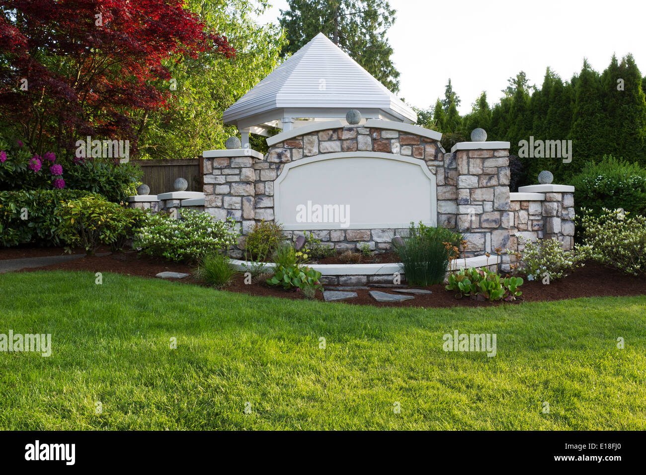 Horizontal evening front view photo of a new white pavilion surround by evergreens, Japanese Red Maple tree and rhododendron Stock Photo
