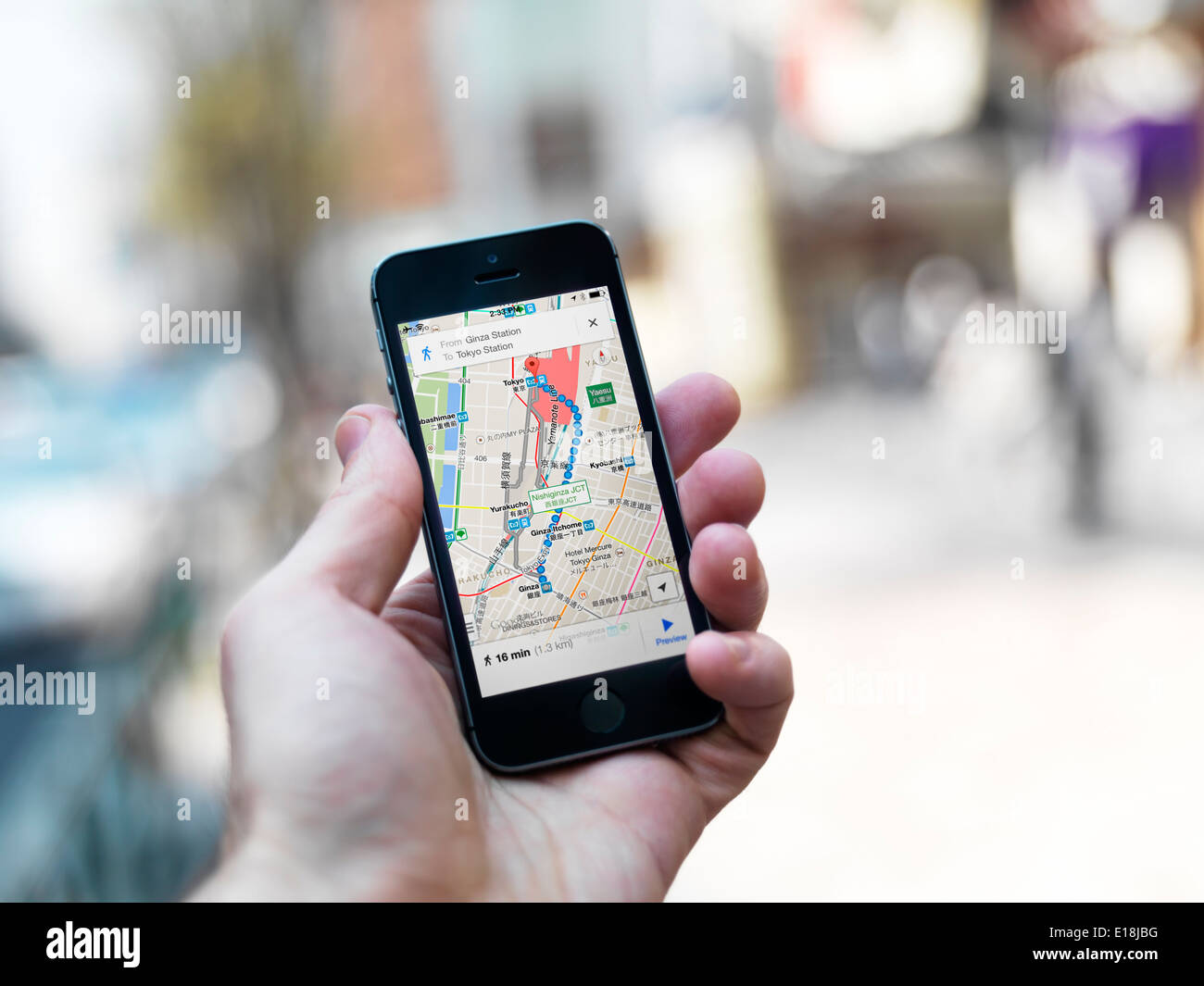 Person hand with iPhone displaying Google maps GPS navigator on streets of Tokyo, Japan. Stock Photo