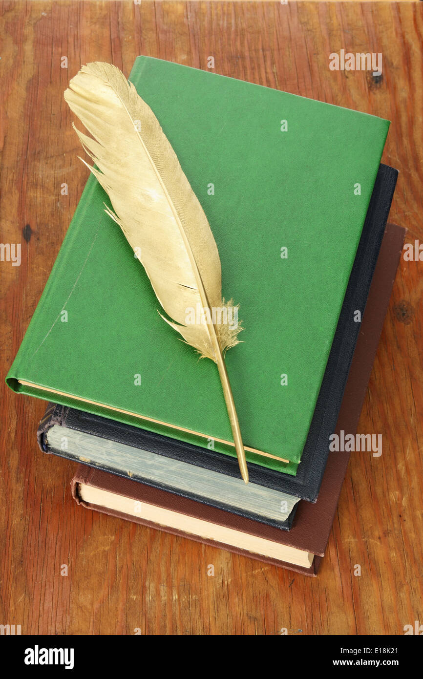Gold quill pen and pile of books on grunge wood board Stock Photo