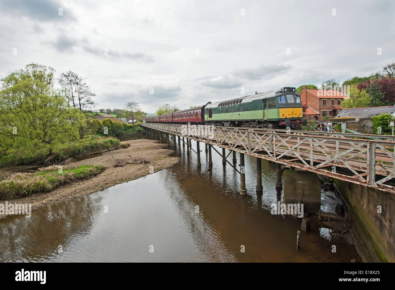 Train in english rural countryside travelling on bridge over river with overcast sky Stock Photo