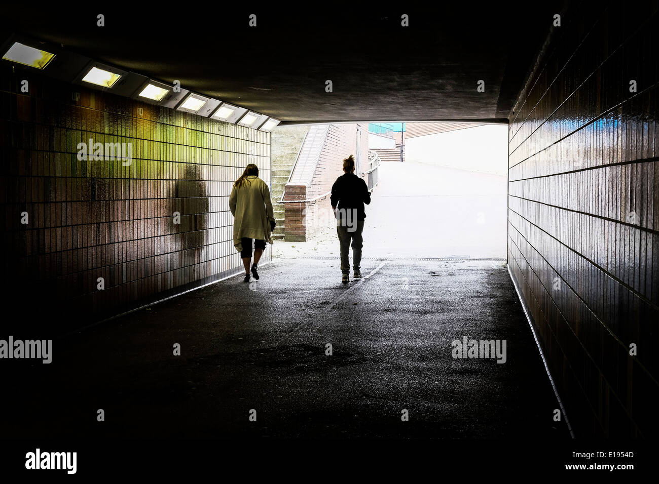 Two people walking through a dark pedestrian subway. Stock Photo
