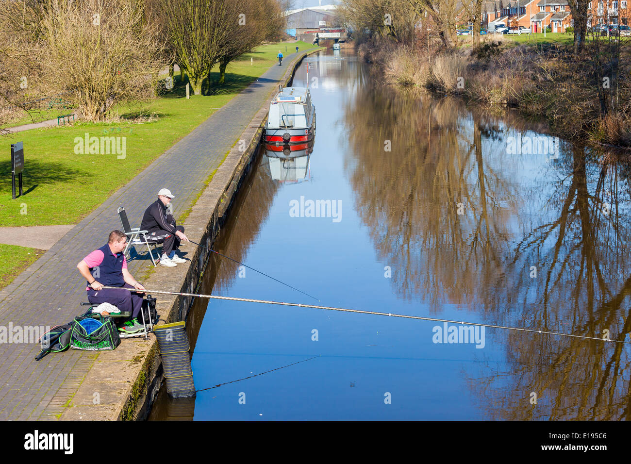 Two young men sitting by the canal side fishing on a sunny spring day, Stoke on Trent,  England, United Kingdom. Stock Photo