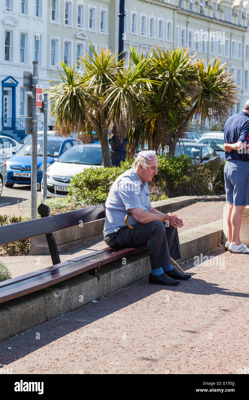Elderly man, sitting on a wooden bench, with knotted handkerchief  on his head, Llandudno, North Wales Wales. Stock Photo