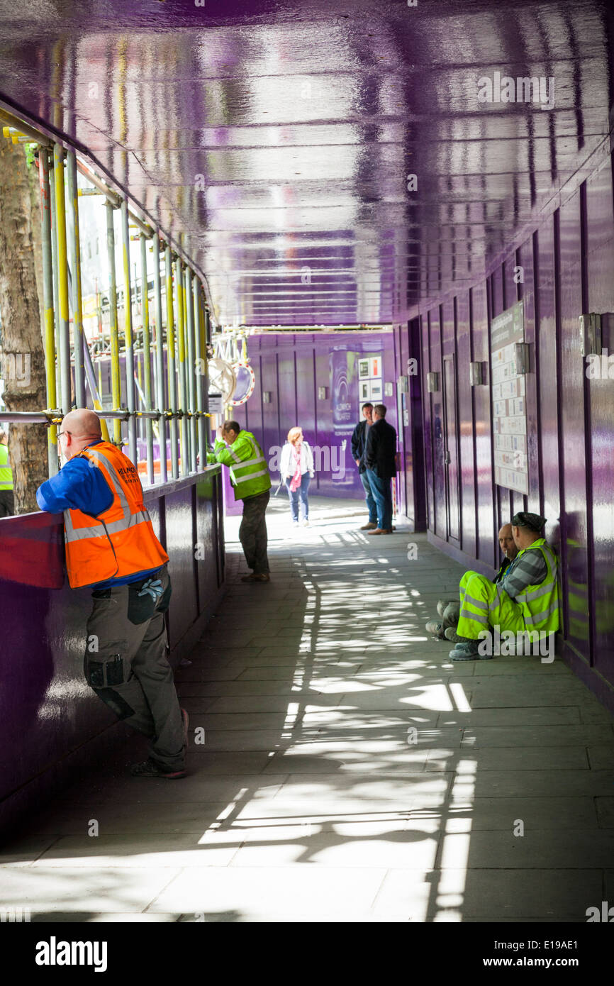 Builders taking a break in boarded safety path by construction site. Stock Photo