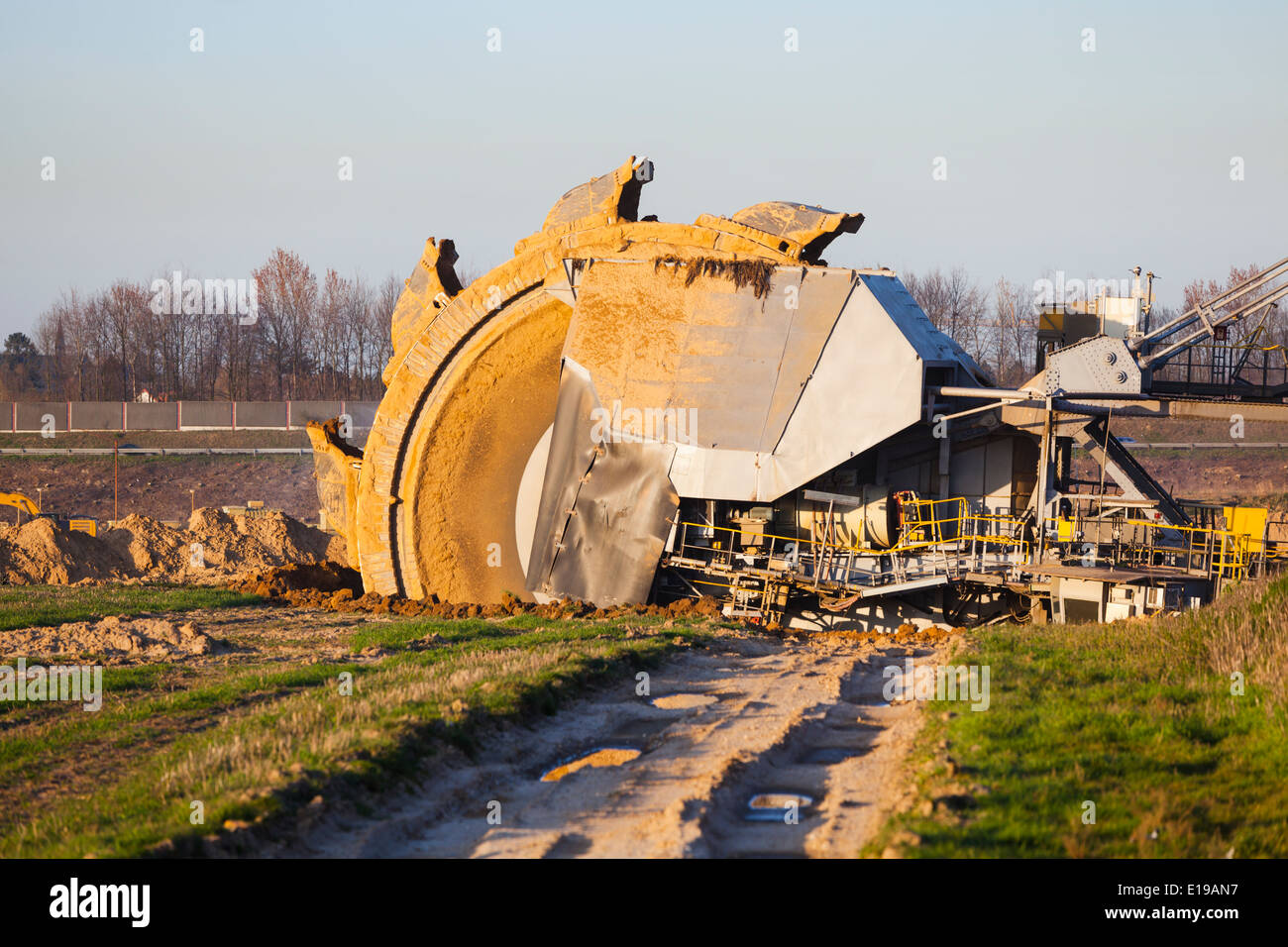 A giant Bucket Wheel Excavator at work in a lignite pit mine with a dirt road leading to it in the foreground Stock Photo