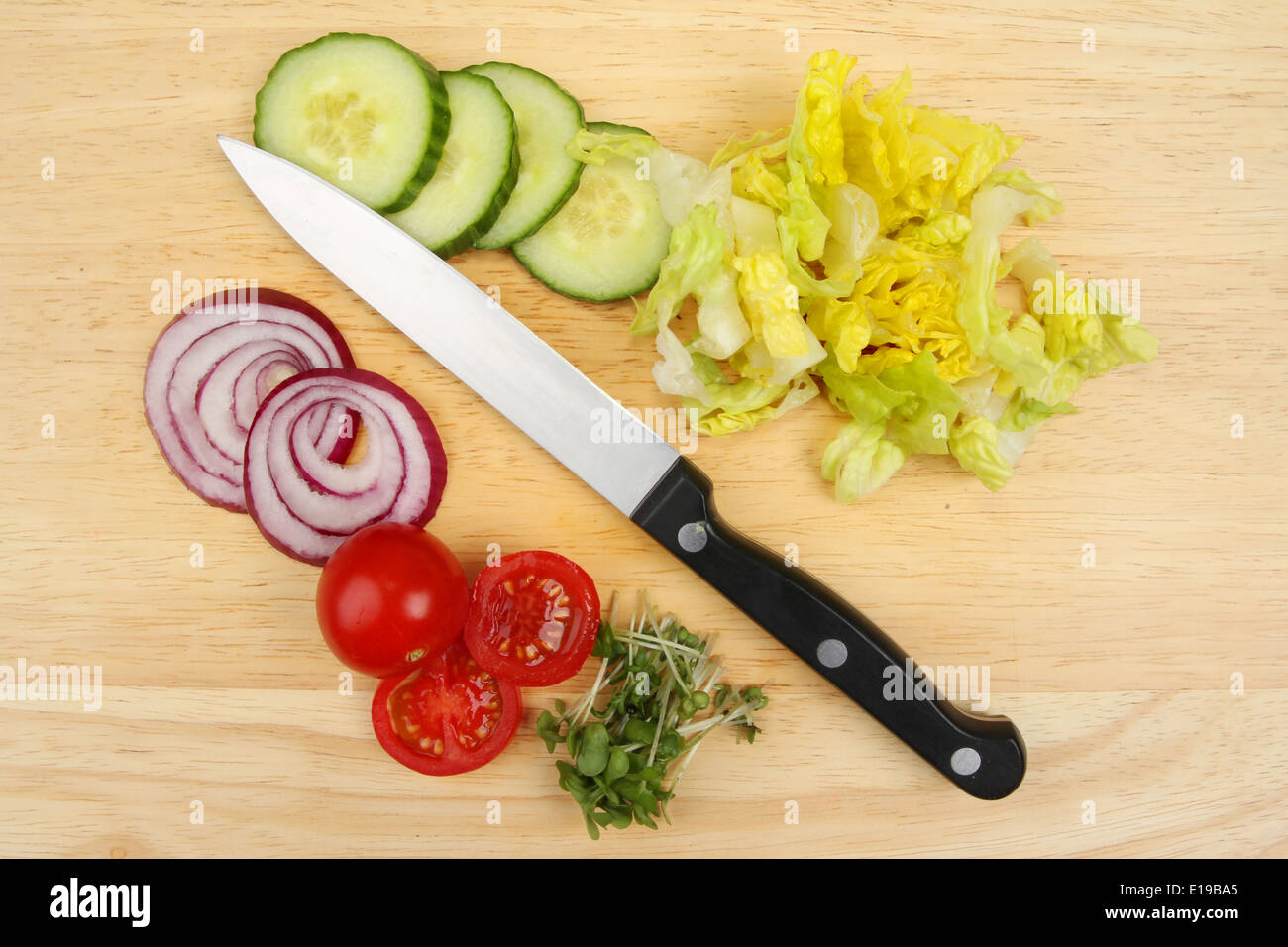 Chopped salad ingredients with a knife on a wooden food preparation board Stock Photo