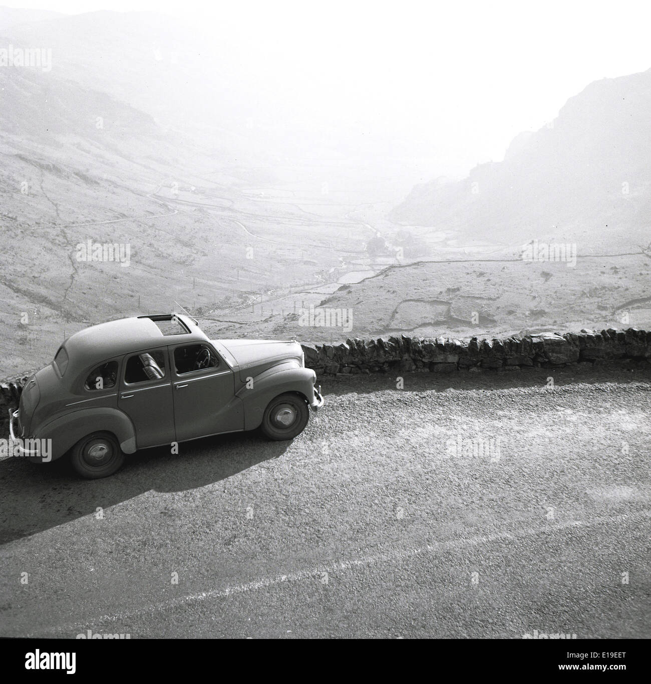 1950s historical picture showing a car parked on the side of a country road with a view down a misty valley, England. Stock Photo