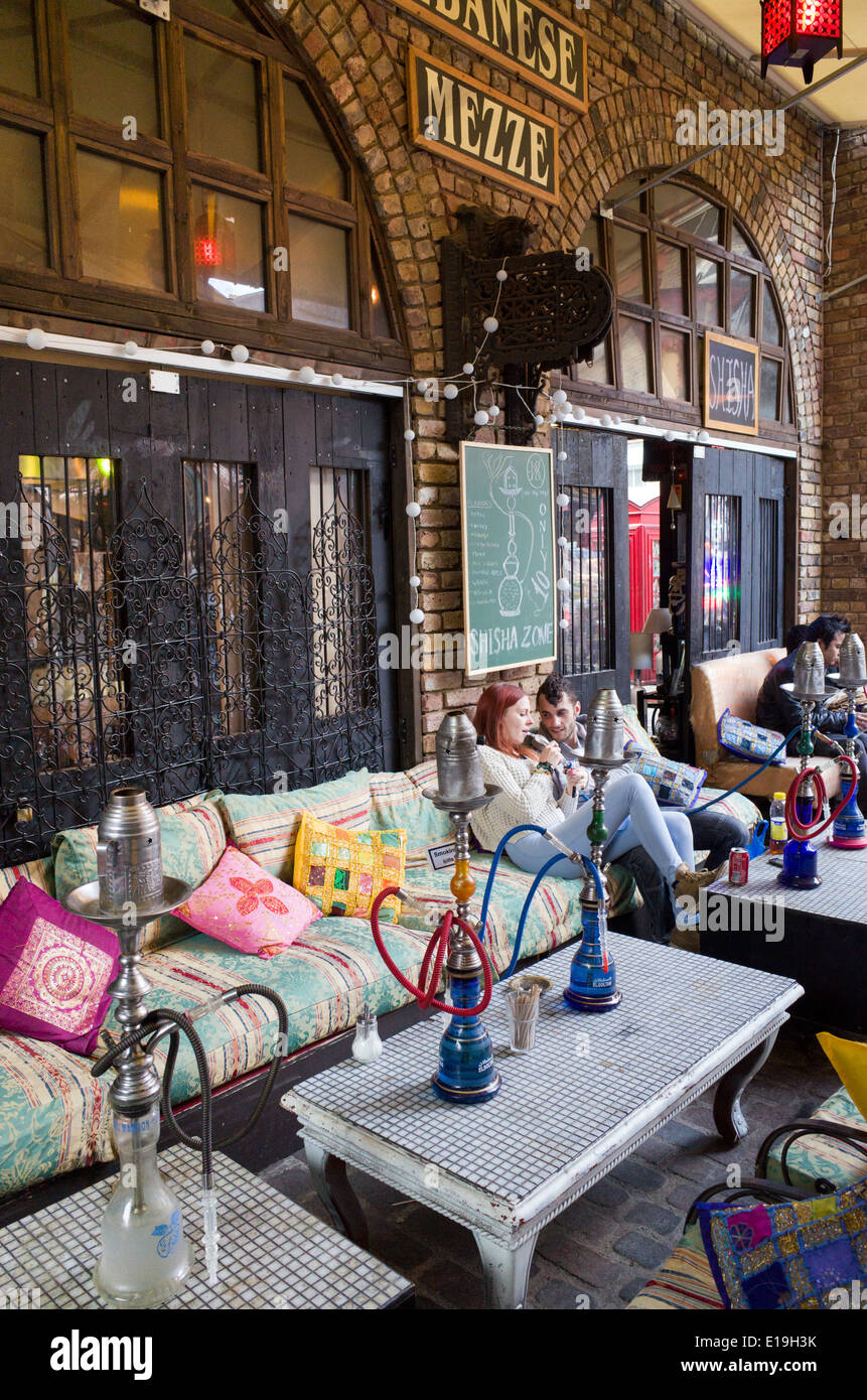 Young people smoking shisha pipes outside Lebanese restaurant in Camden Stables Market, London, England, UK Stock Photo