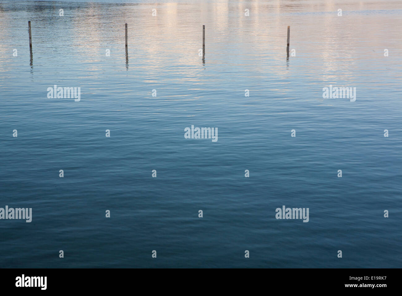 Reflections of the cloudy sky in the sea, four groynes are sticking out of the water. Stock Photo