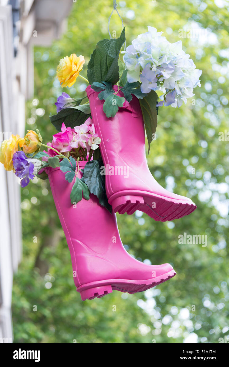 A pair of pink wellington boots used as flower containers hanging up outside a shop near the Chelsea Flower Show UK Stock Photo