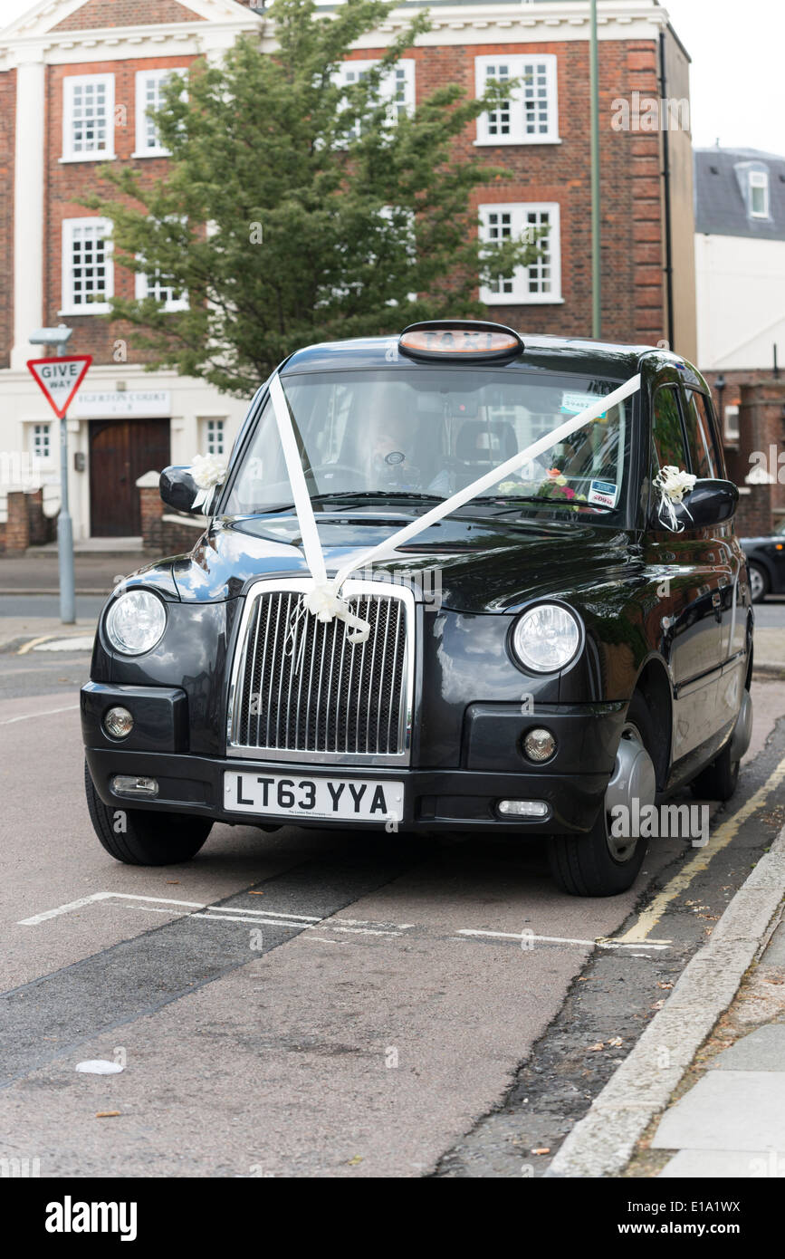 A black cab London taxi with decorative white wedding ribbons attached waiting outside a wedding venue. Stock Photo