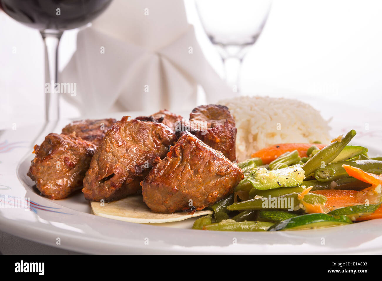 Macro shot of shish kebabs garnished with vegetables and rice pilaf, napkin and vine glass on the background Stock Photo