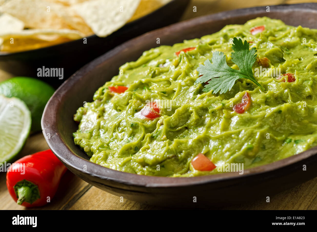 A bowl of creamy guacamole dip with peppers, tomato, cilantro, and lime. Stock Photo