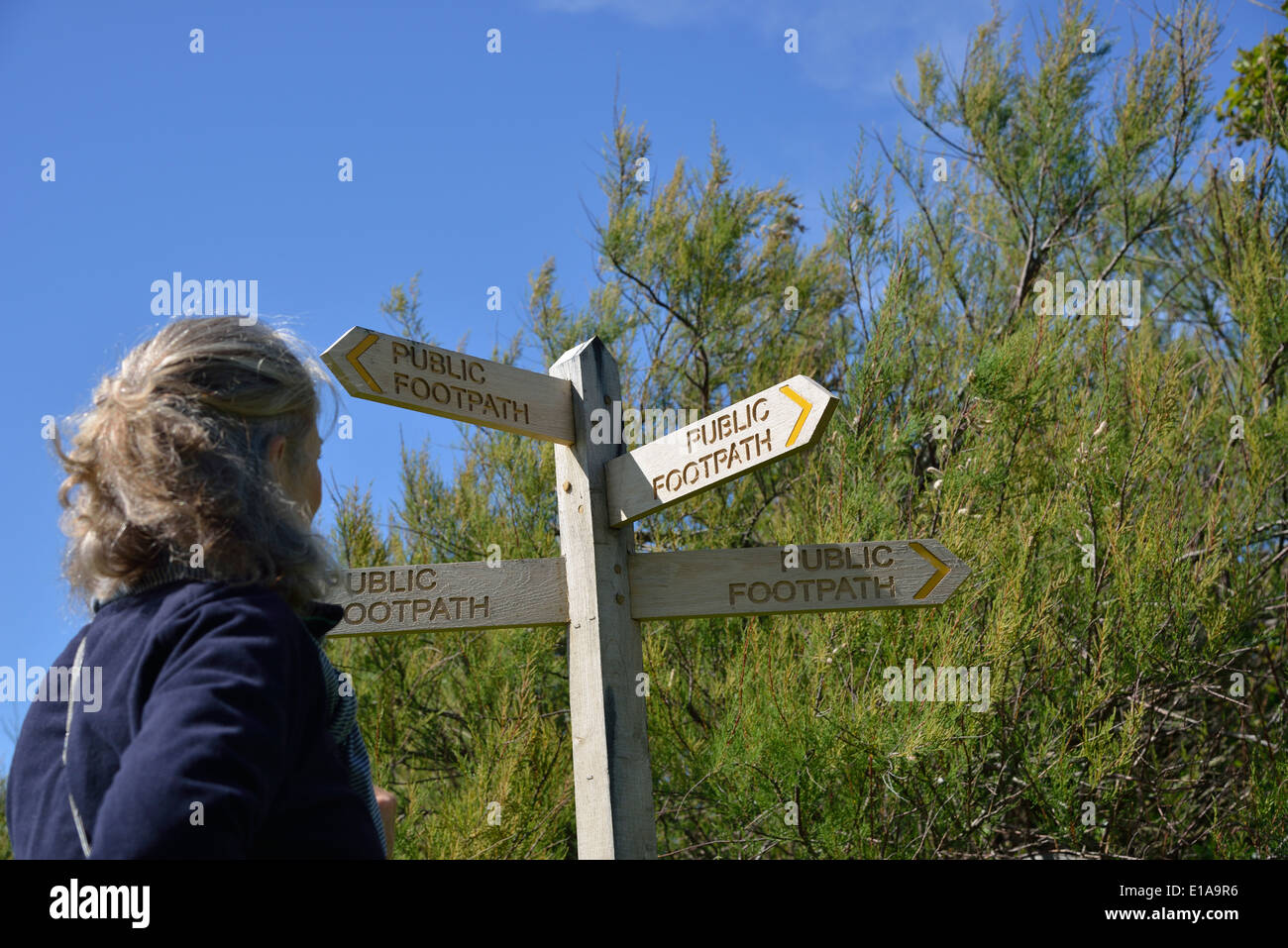 Woman making a choice of direction standing beside a public foothpath sign at Snow Hill, West Wittering, West Sussex,UK Stock Photo