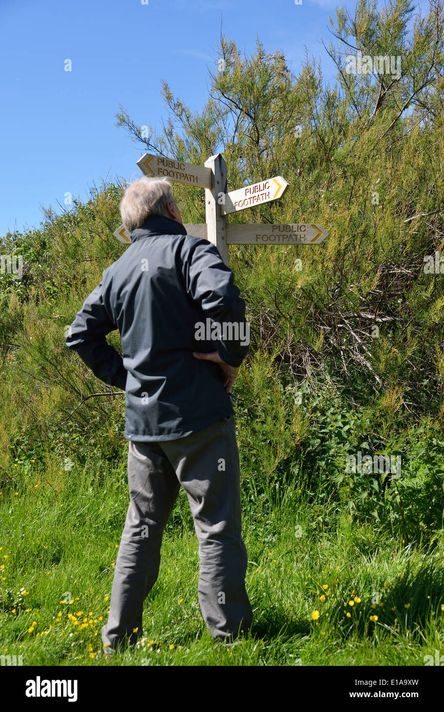 Man making a choice of direction standing beside a wooden public foothpath signpost (finger post)  at Snow Hill, West Wittering, West Sussex,UK Stock Photo