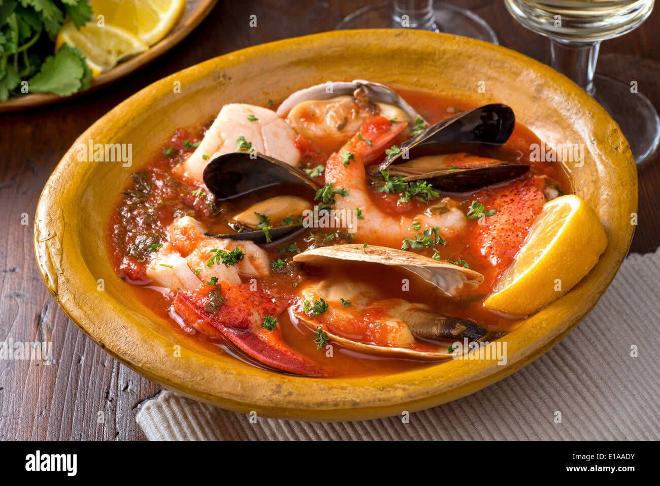 A hearty bowl of rustic mediterranean seafood stew with lobster, shrimp, mussels, clams, scallops, and white fish. Stock Photo