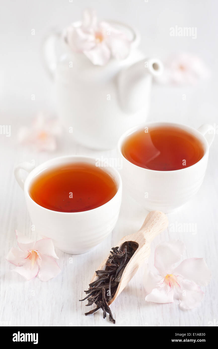 Oolong tea in a scoop, cups and teapot with light rose rhododendron