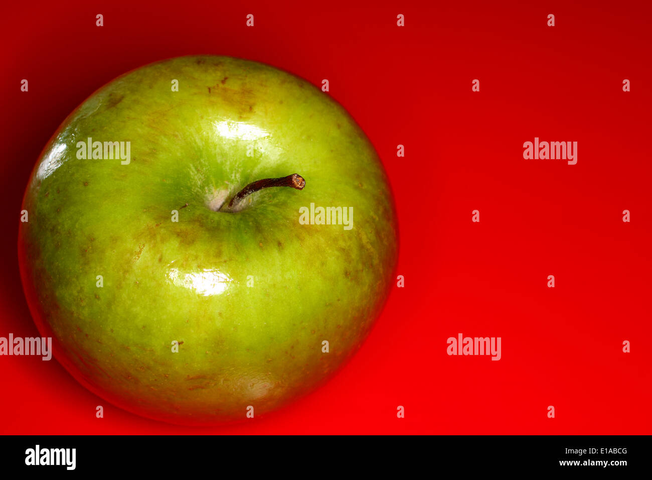 Green apple on a red background with room for copy Stock Photo - Alamy