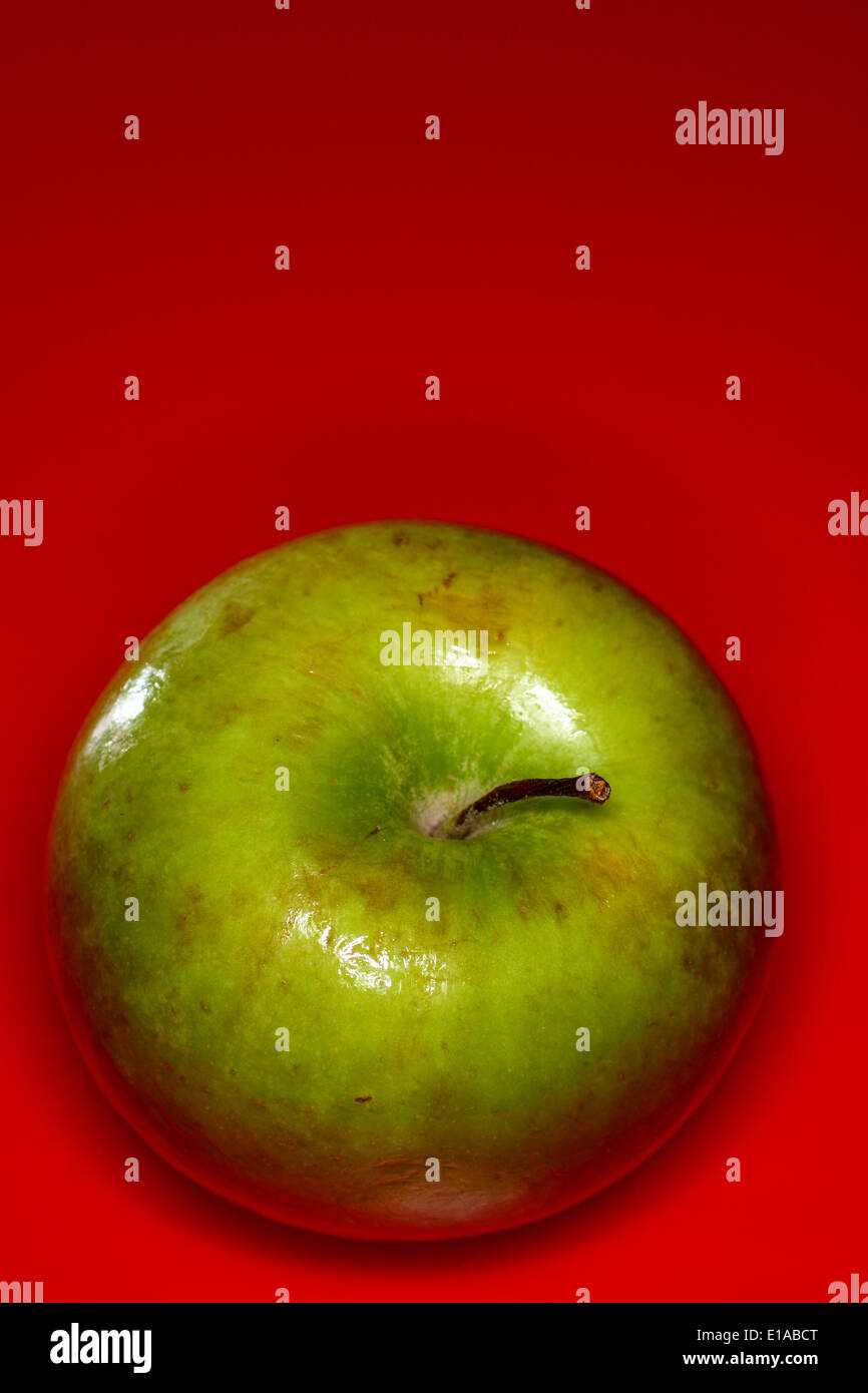 Green apple on a red background with room for copy Stock Photo - Alamy