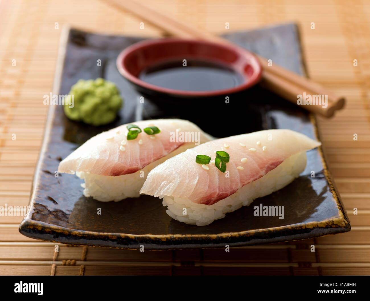 A delicious white fish nigiri-zushi with rice, wasabi paste, and japanese soy garnished with green onion and sesame seeds. Stock Photo