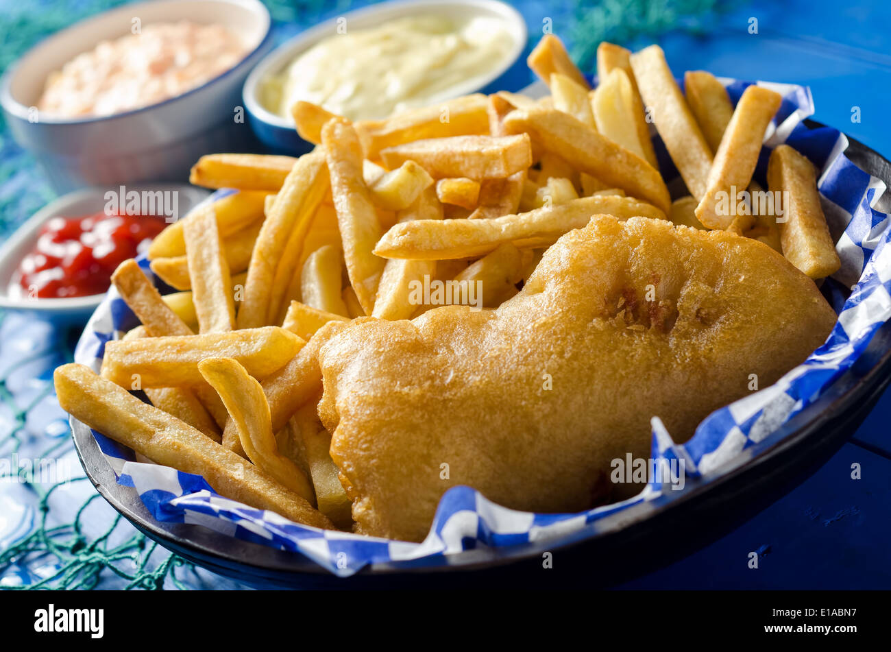 A golden delicious batter fried piece of fish with french fries, tartar sauce, coleslaw, and ketchup. Stock Photo