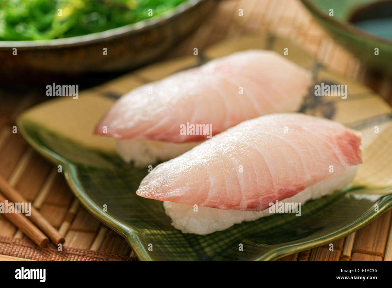 A delicious white fish nigiri-zushi with rice, wasabi paste, and japanese soy served with seaweed salad. Stock Photo